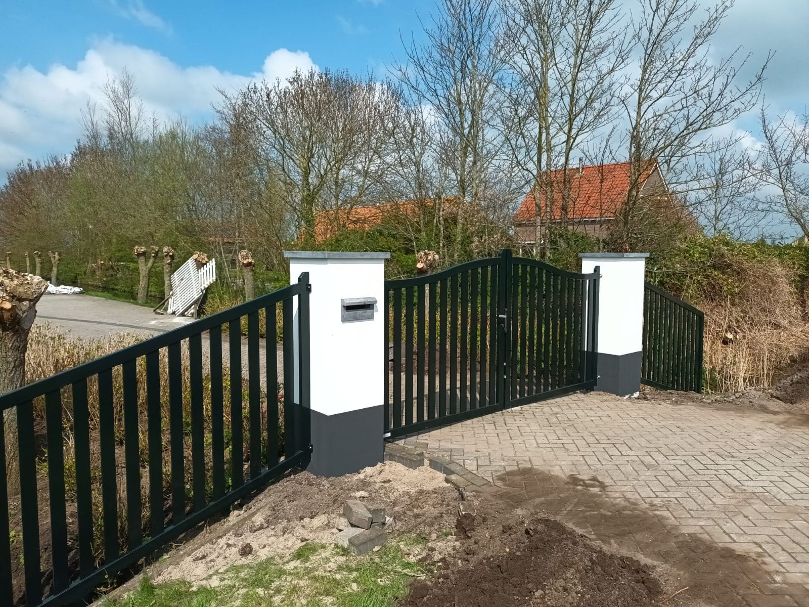 Dubbele stalen inrijpoort met boog tussen witte poeren en bijpassend hekwerk