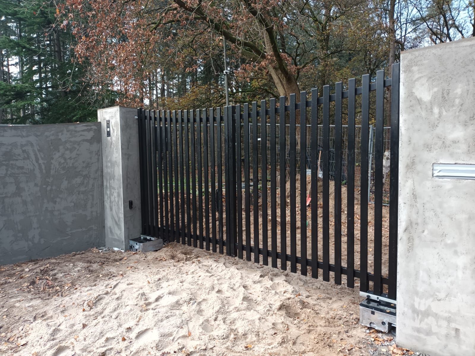 Zwarte stalen draaipoort met spijlen tussen betonnen muren