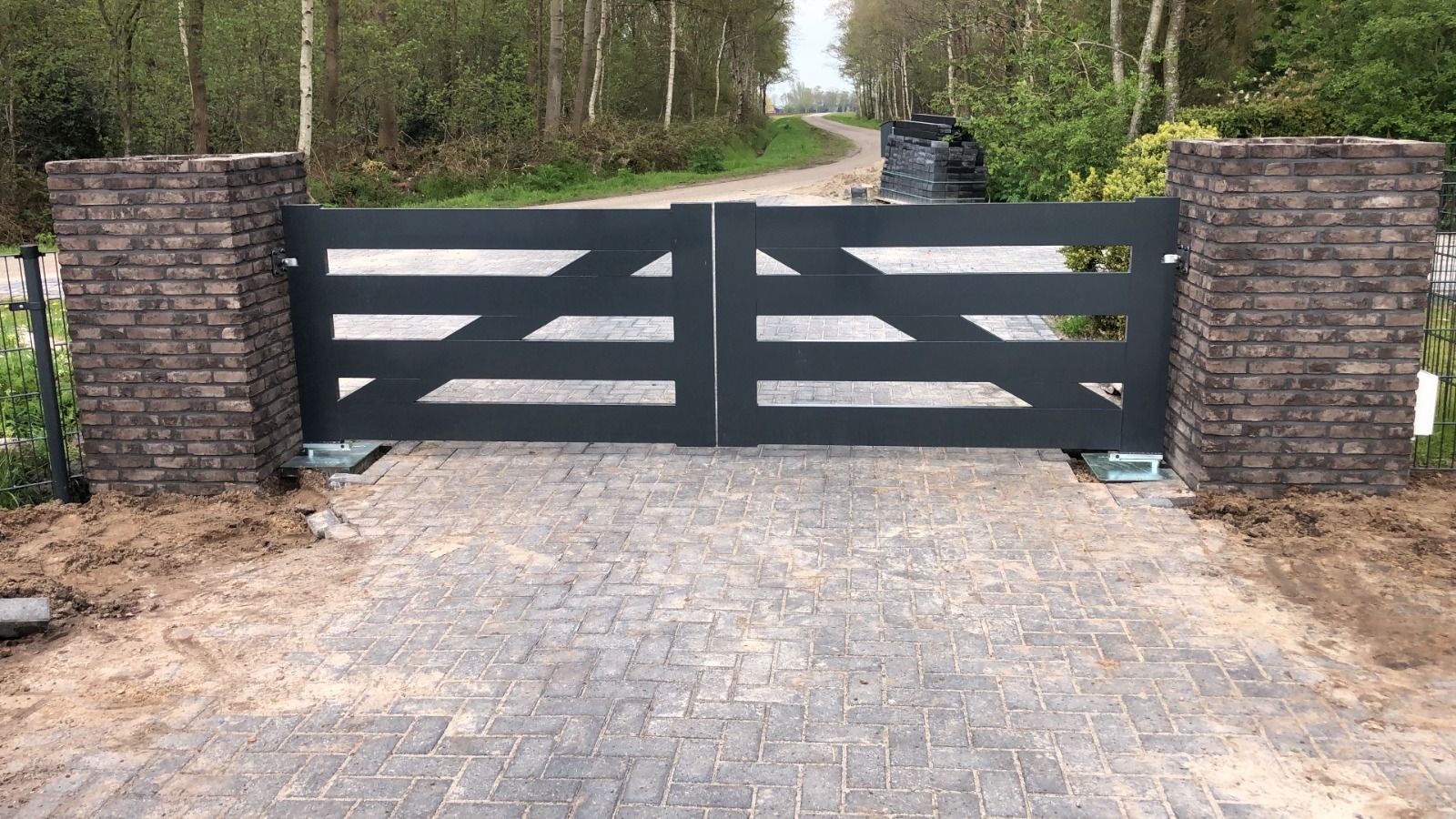 Dubbele stalen inrijpoort tussen gemetselde poeren op een oprit