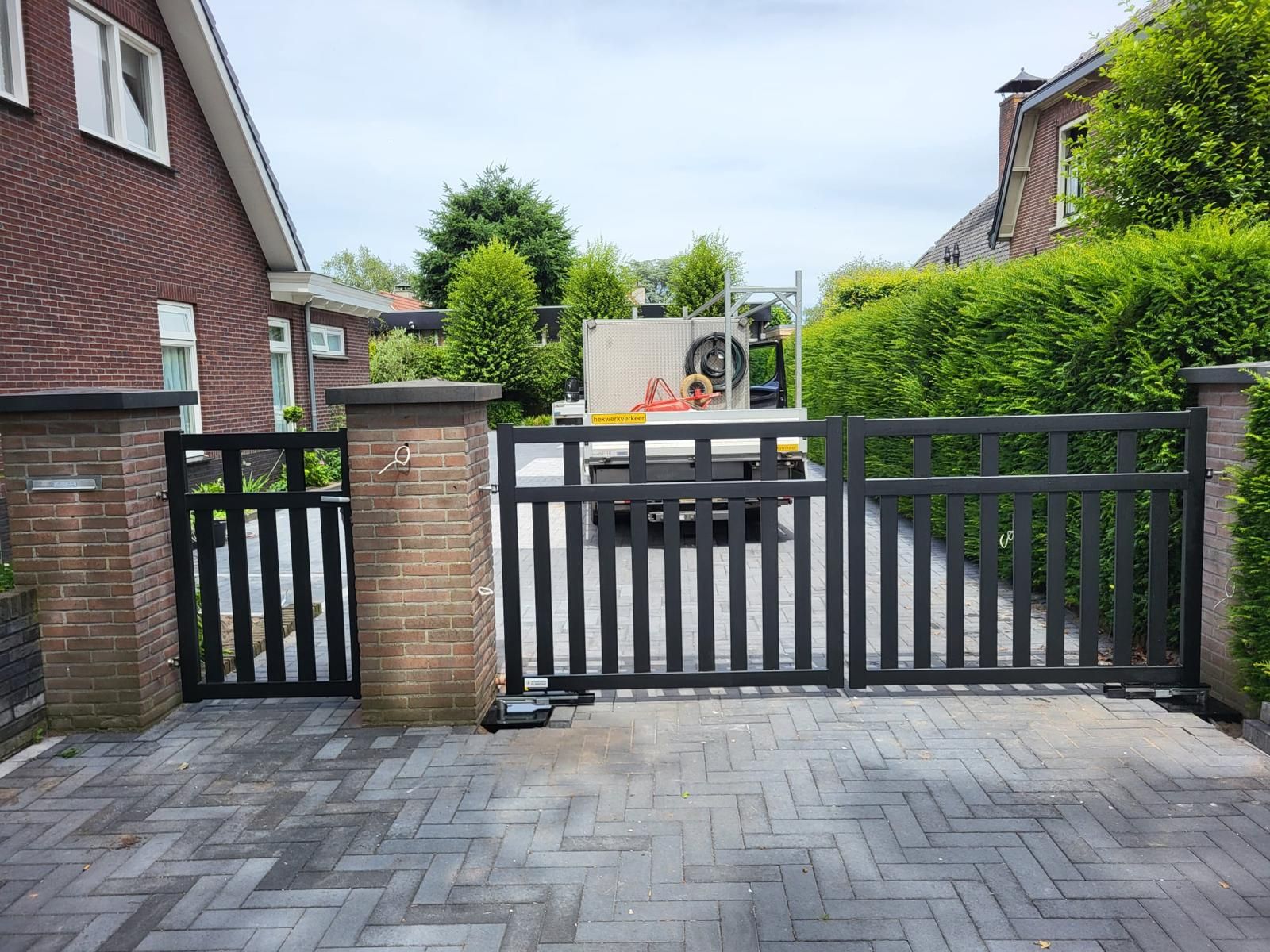Stalen inrijpoort met looppoort tussen gemetselde poeren