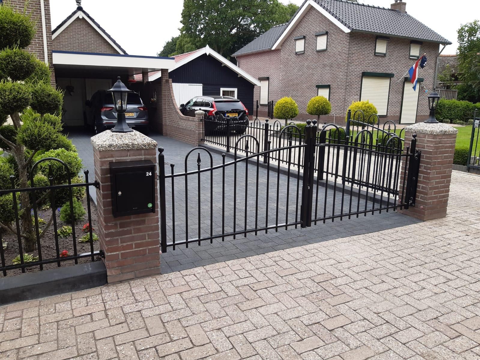 Dubbele stalen sierpoort tussen gemetselde pilaren met brievenbus en lantaarn